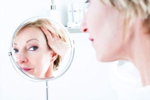 An image of a women inspecting her face in a close up mirror