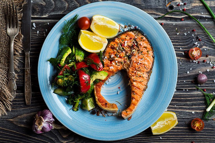 An image of an appetising salmon dish with salad and sliced lemon on a blue plate