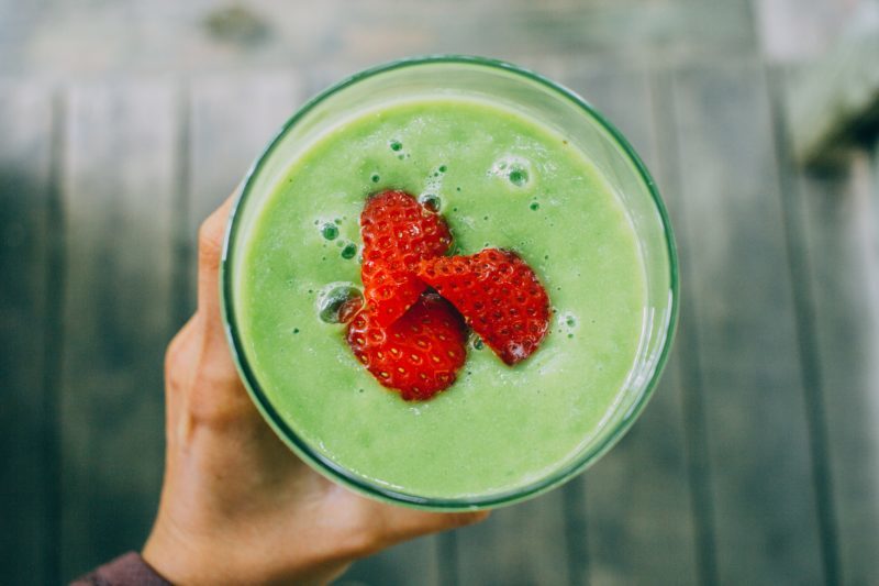 An image green smoothie toped with a sliced strawberry