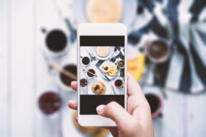 An image of a woman taking an instagram picture of an array of photogenic food and drinks