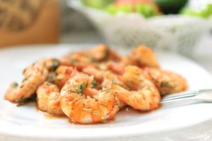 An image of Fried black tiger prawns with herbs and spices on a white plate.