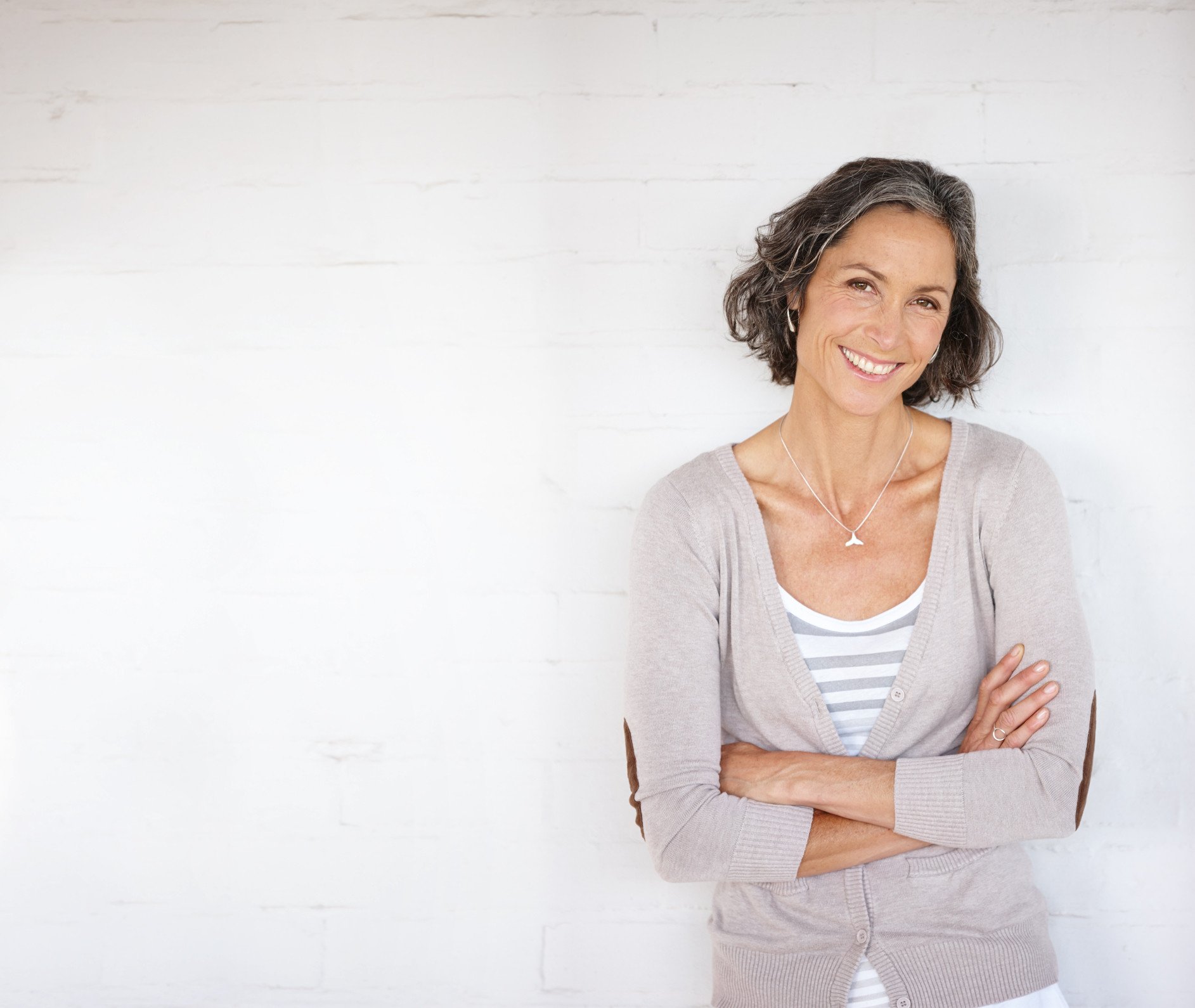 Portrait of a mature woman smiling, while standing against a wall.