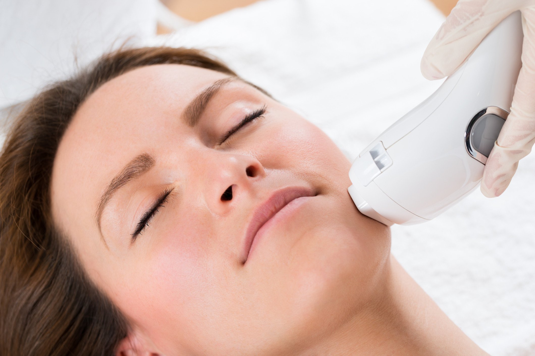 Close up of a beautican using a rejuvenating skin device on a young woman.