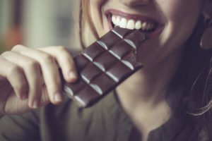 Close up of a woman eating dark chocolate for an article about healthy foods for glowing skin