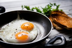 An image of two fried eggs in a pan next to some toast.