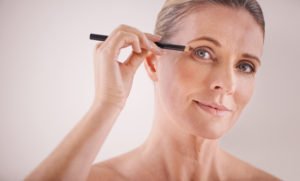 image of an older woman using a liner pencil for an article about how to get thicker eyebrows