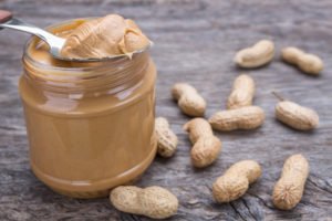 Image of a jar of peanut butter with nuts. On wooden texture.