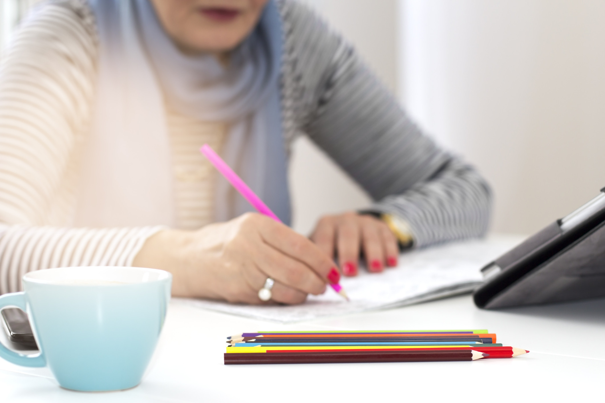 Close-up of senior woman sitting at a desk in the office and colouring an adult colouring book.