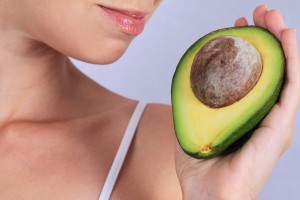 Image of a woman holding half the superfood, avocado close to her face.