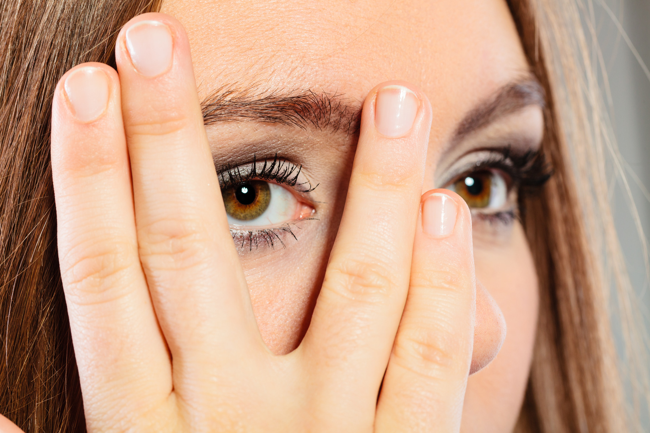 Image of an exhausted woman covering her eye bags with her hands.