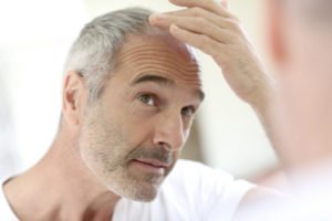 A man apprehensively looks and touches his receding hair line in the mirror