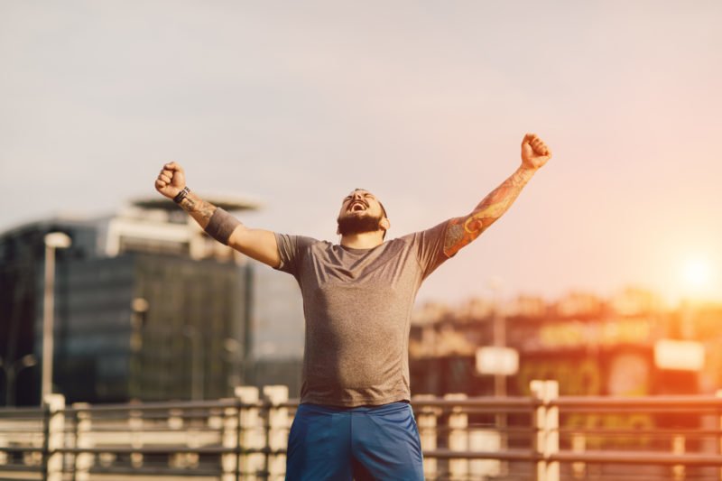 An image of a male runner raising his arms and looking up to the sky in celebration