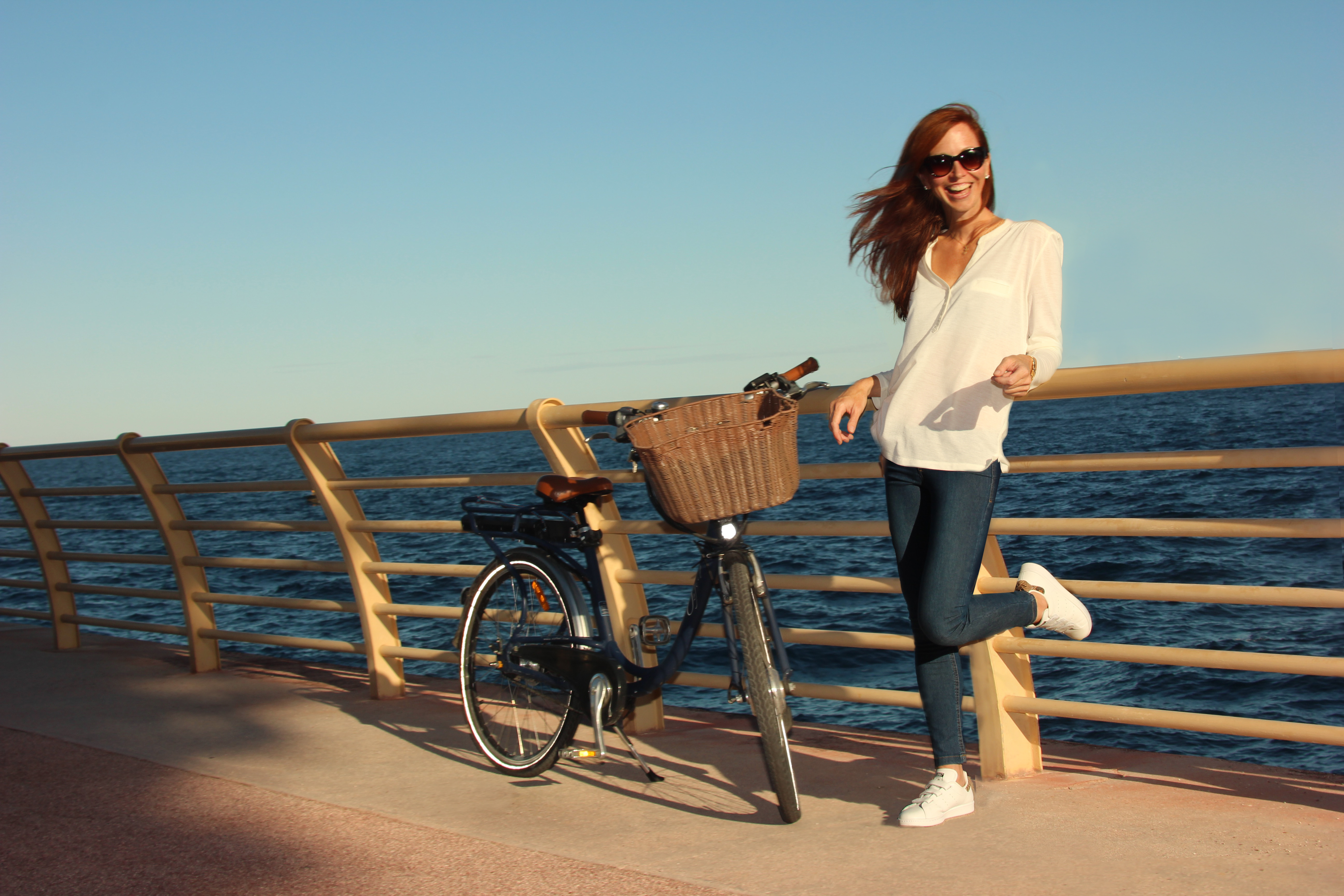 An image of Dr Sara Palmer Hussey posing with her bike on a fence overlooking the ocean.