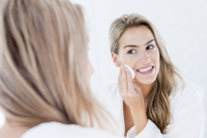 An image of a woman looking in a mirror cleansing her skin with a cotton pad.