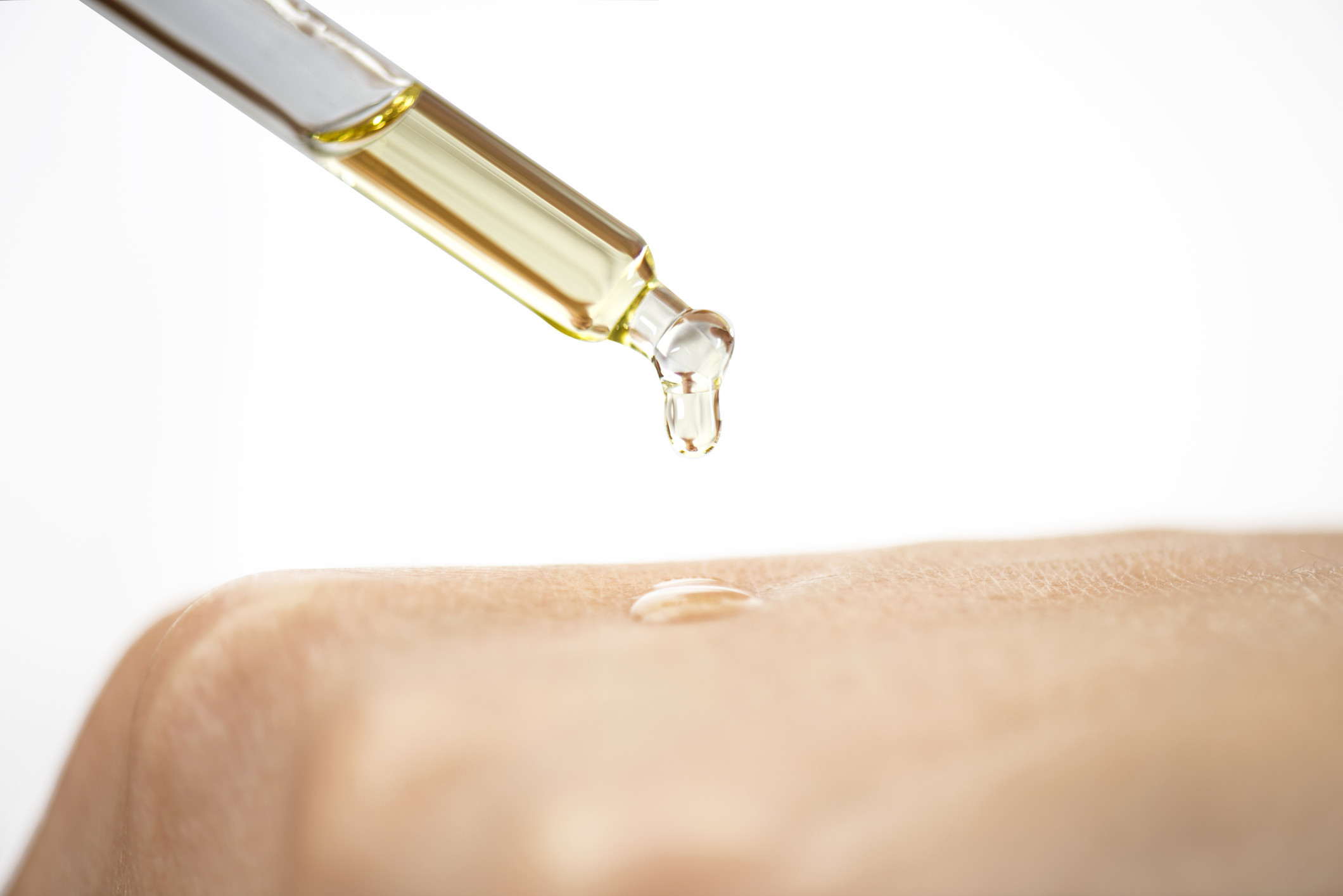 A close up of a woman using a pipette of anti-ageing serum on her hand.