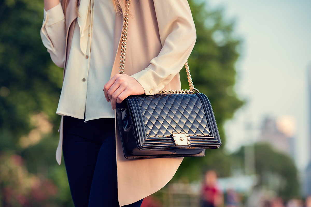 A close up of a woman walking down the park in summer holding a stylish handbag.