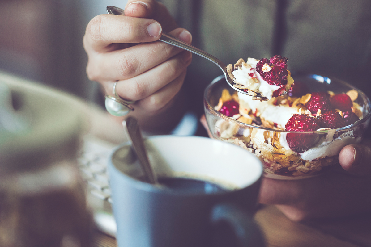 An image of a woman eating a healthy breakfast of yogurt, fruit and granola.