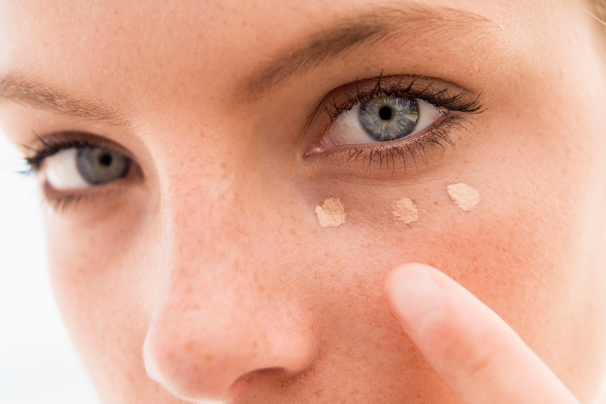 An image of a woman applying dark circle concealer to her face.