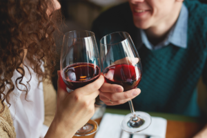 An image of a couple on a date chinking their red wine glasses.