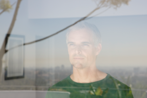 An image of a depressed middle aged man looking through a window.