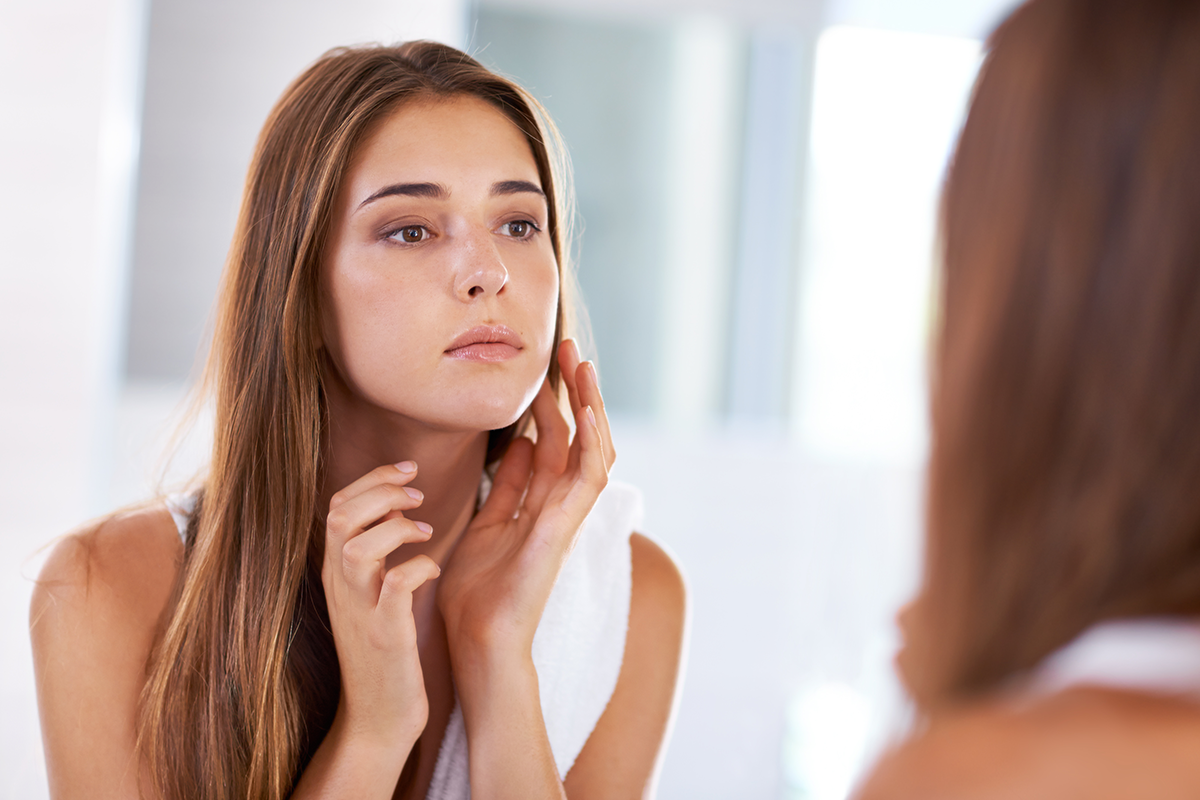 An image of a woman inspecting her face in the mirror.