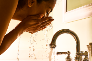 An image of a middle aged woman washing her face with water.