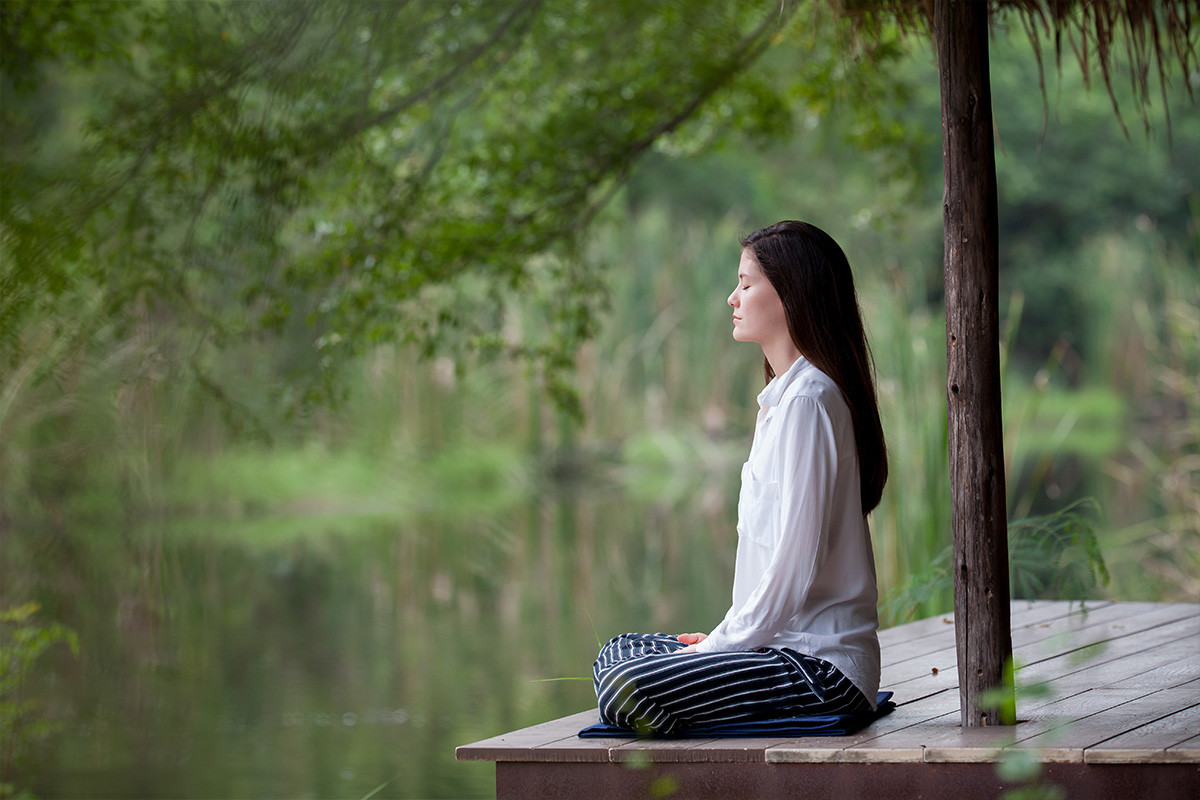 An image of a middle aged woman peacefully relaxing by a lake.