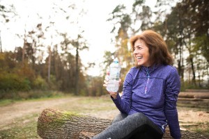 An image of a middle aged woman staying hydrated by drinking plenty of water to keep the lymphatic system fluid.