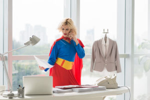 An image of a lady dressed in a superwoman outfit while multi-tasking in her office.