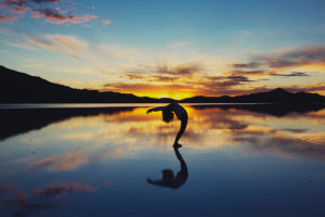 An image of a woman on a beautiful beach doing yoga at sunset.