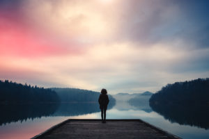 An image of a woman managing her stress by going on a peaceful walk by the lake.