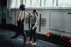 An image of a mature woman working out with an exercise ball and the support of a personal trainer.