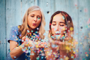 An image of a mature woman and her daughter blowing confetti to celebrate new year.