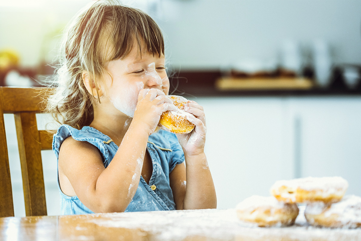 An image of a happy young girl eating doughnuts.