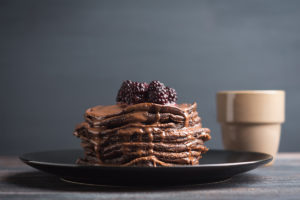 An image of a stack of chocolate pancakes topped with blackberries.