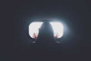 An abstract image of anxiety - a woman trapped in a dark room looking out of a small window.