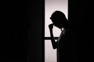 An image of a silhouette of a depressed woman holding the arch of her nose in lament.