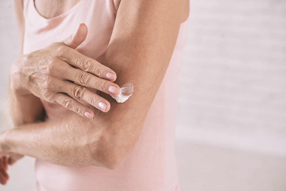 An image of a mature woman applying moisturiser to her arm.