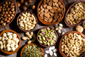 Top view of a rustic wood table filled with a large assortment of nuts like pistachios, hazelnut, pine nut, almonds, pumpkin seeds, peanuts, cashew and walnuts.