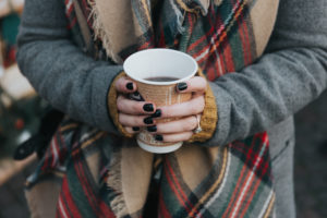 close up of girl with black nail varnish and diamond ring holding a warm drink with a tartan scarf and grey coat