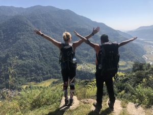 louise with a man carrying backpacks with their arms in the air overlooking the mountains in Nepal