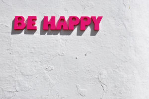 rustic wall painted white with the pink words 'be happy' stuck on the wall