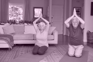 elderly man and woman doing yoga together on yoga mats in their front room