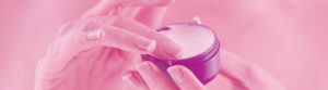 well manicured hands of a woman touching her face cream with a pink wash filter