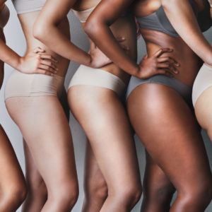 studio shot of unrecognisable diverse women in underwear posing against a grey wall