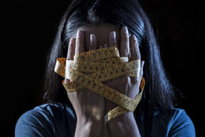 woman covering har face with her hands that are wrapped in a yellow tape measure