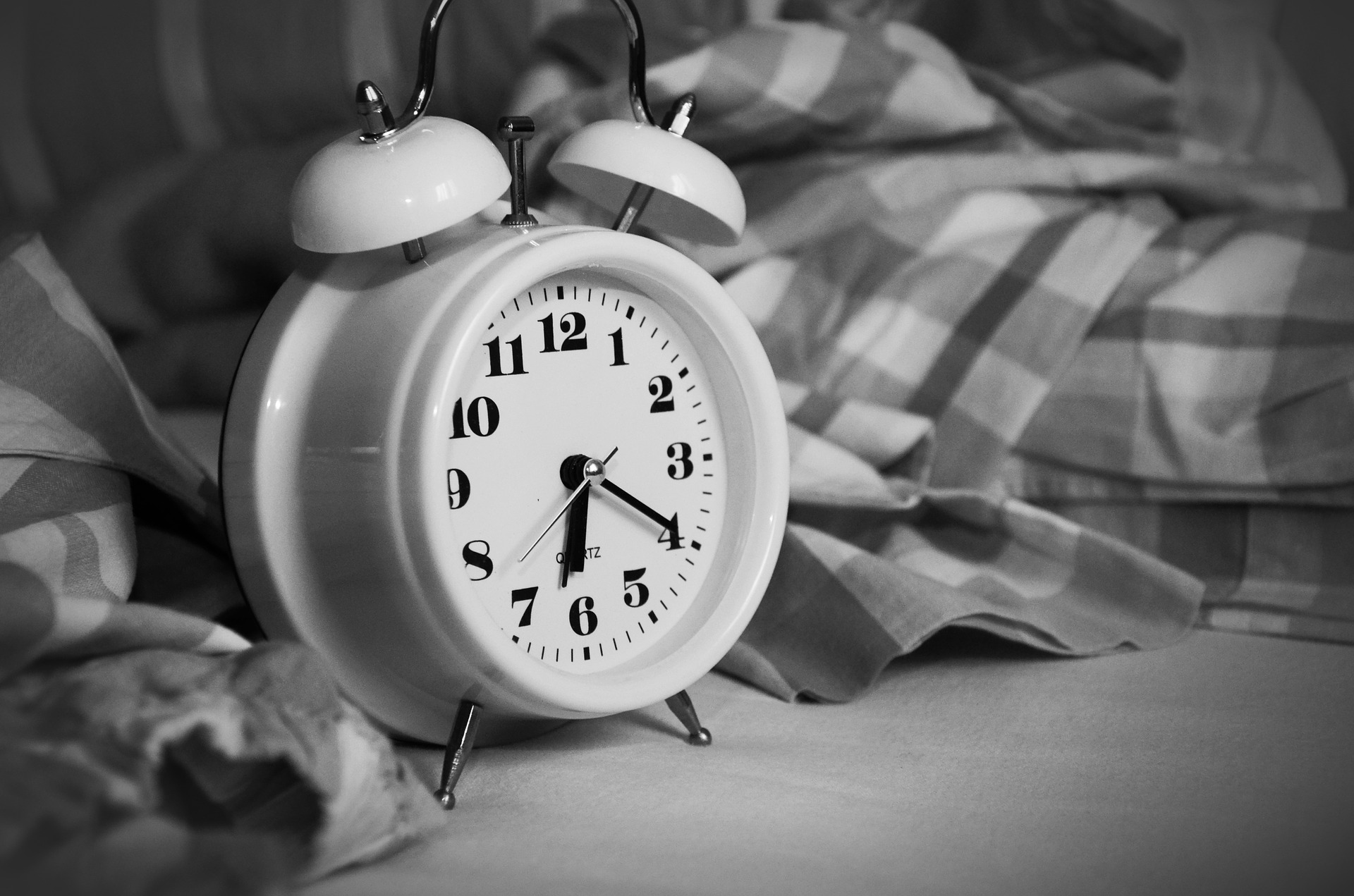 black and white photo of an alarm clock next to an un-made bed