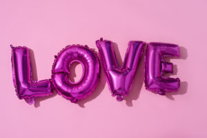 purple helium balloons that spell Love on a pink background