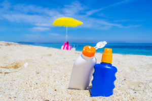 bright photo of two bottles of sun lotion in the sand on a beach