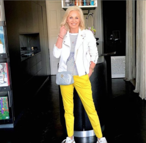 stylish mature woman in bright yellow trousers and white leather jacket